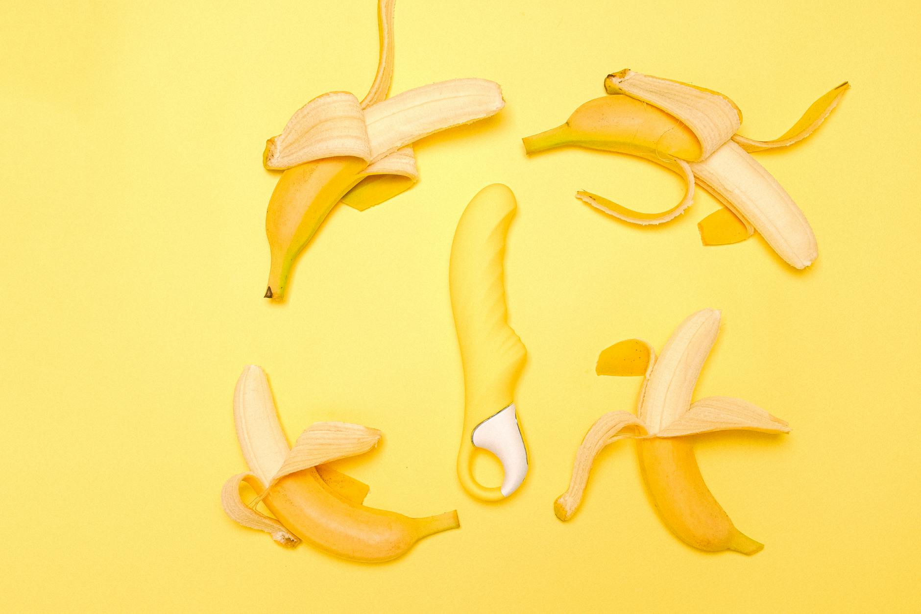 Yellow silicone lemon clitoral vibrator surrounded by peeled bananas on a yellow background.