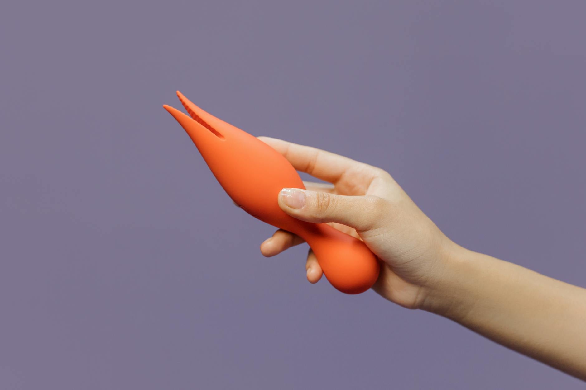 A hand holding a lemon-colored clitoral vibrator against a purple backdrop, representing reconnecting with pleasure.