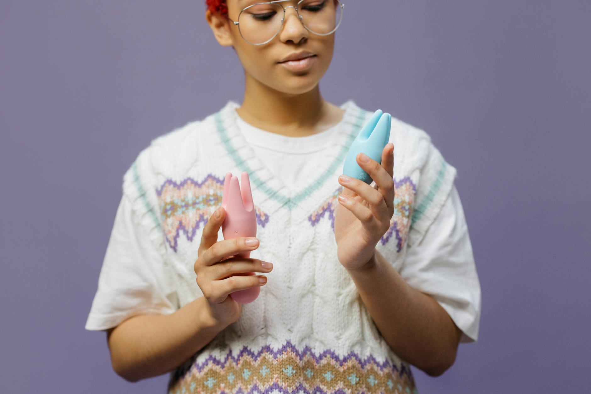 Woman holding blue and pink silicone vibrators thoughtfully during recovery.